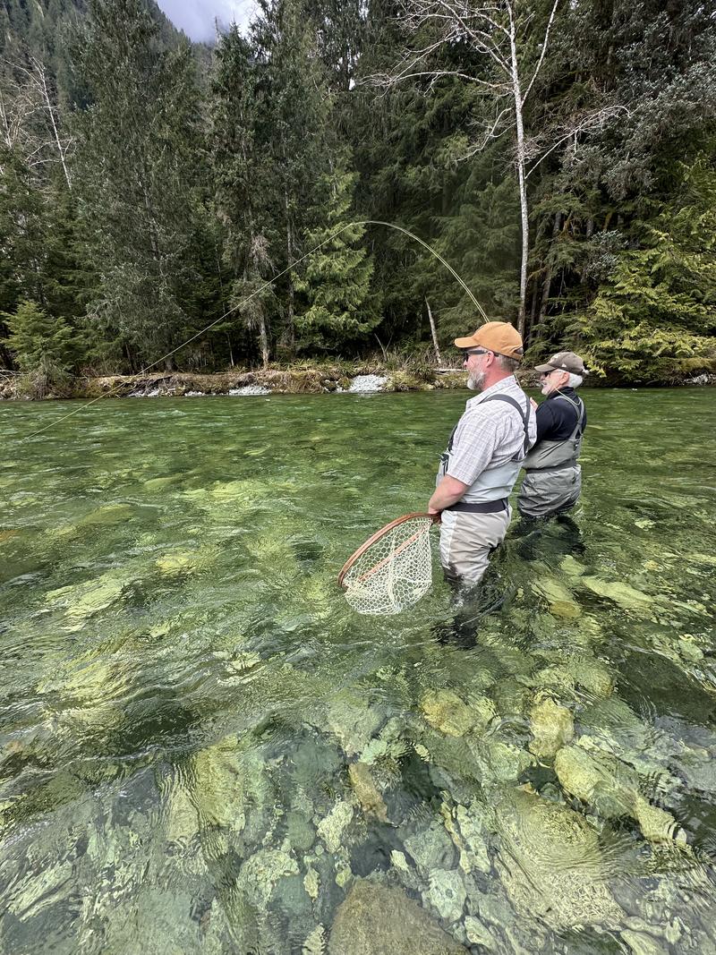 Two people wading in a clear, rocky river, fly fishing.