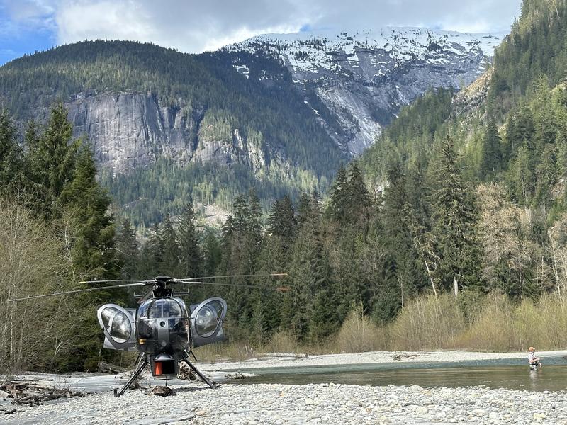 A helicopter landed on a sandy beach with forested mountains in the background.