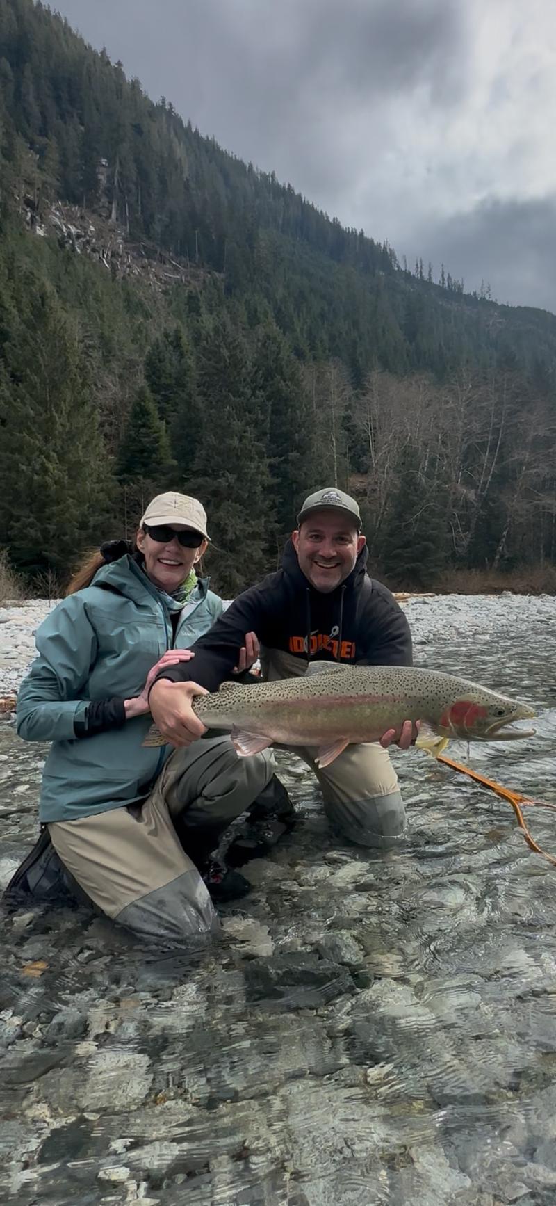Two anglers kneeling in a river holding a large fish.