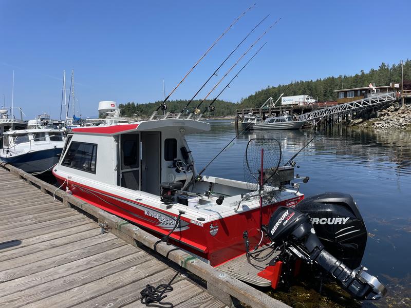 A red and white fishing boat docked at a wooden pier with fishing rods set up.