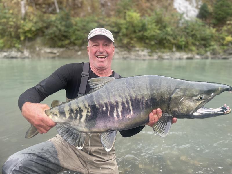 A smiling man holding a large salmon in a river.
