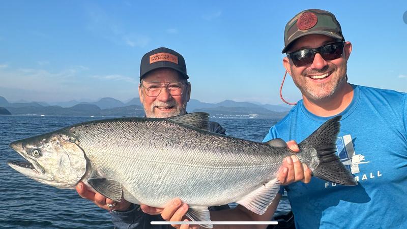 A close-up of a man holding a large salmon near the water.