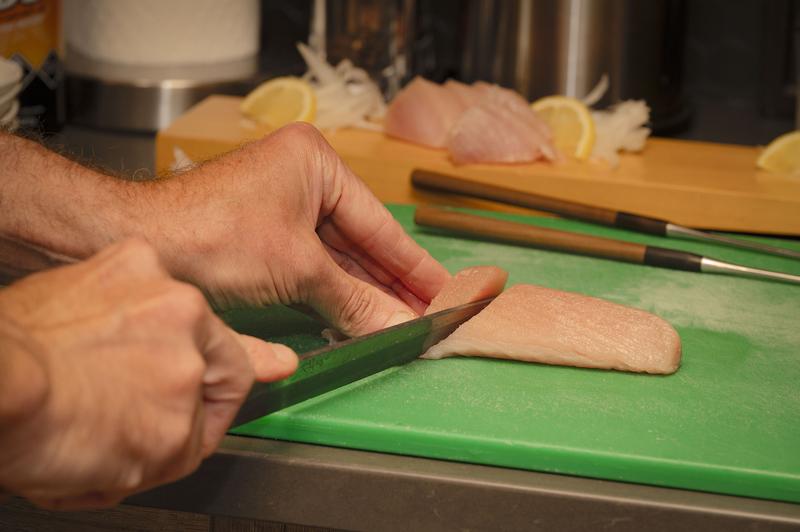 Close-up of hands slicing raw fish on a green cutting board.
